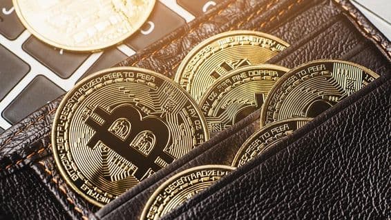 Moeda Bitcoin em uma carteira de couro sobre um teclado de computador.