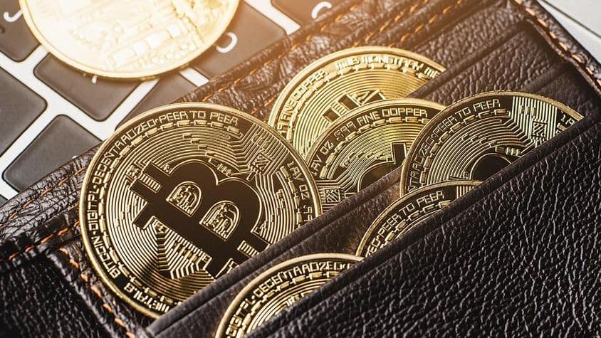 Moeda Bitcoin em uma carteira de couro sobre um teclado de computador.