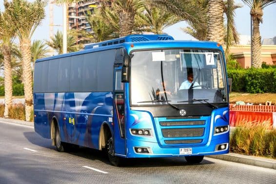 Ônibus azul de Dubai com palmeiras ao fundo.