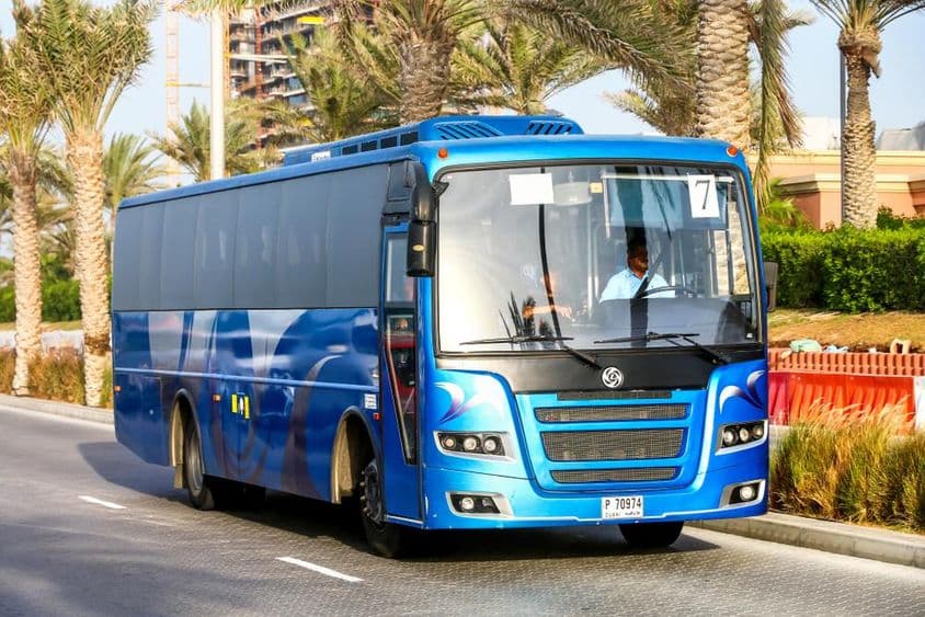 Ônibus azul de Dubai com palmeiras ao fundo.
