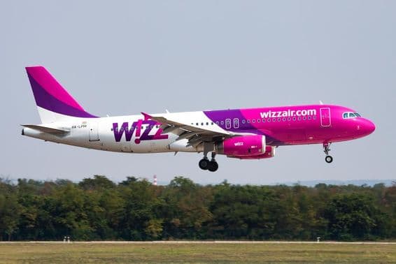 Avião da Wizz Air voando em baixa altitude com uma floresta ao fundo.