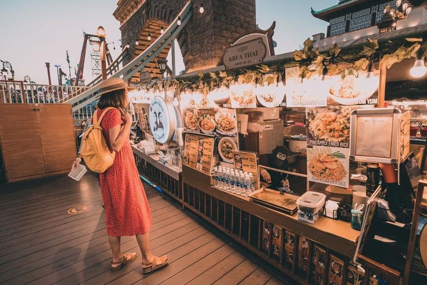 Mulher em vestido vermelho de bolinhas olhando para cozinhas nacionais no Global Village de Dubai.