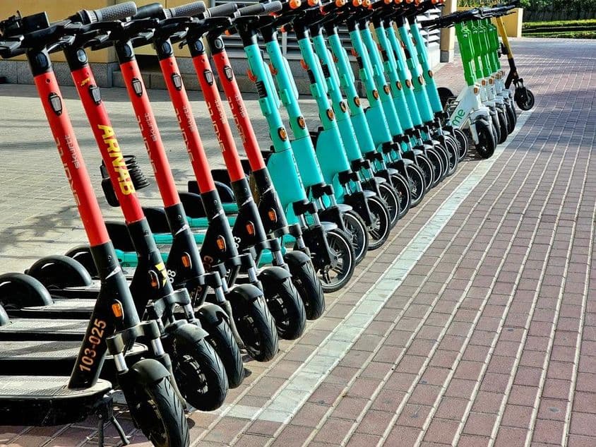 Scooters vermelhas, azuis e verdes aguardando em suas áreas de estacionamento.