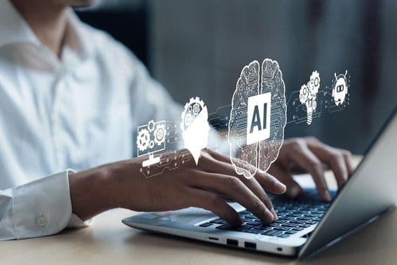 Projeção sobre um notebook mostrando um cérebro de IA e outros elementos. Uma mão humana trabalhando no computador.