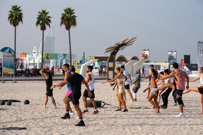Um grupo de pessoas se exercitando em uma praia de areia durante o Desafio de Fitness Dubai.