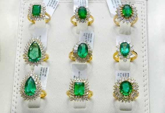 Anéis de esmeralda rodeados por diamantes em uma aliança de ouro.