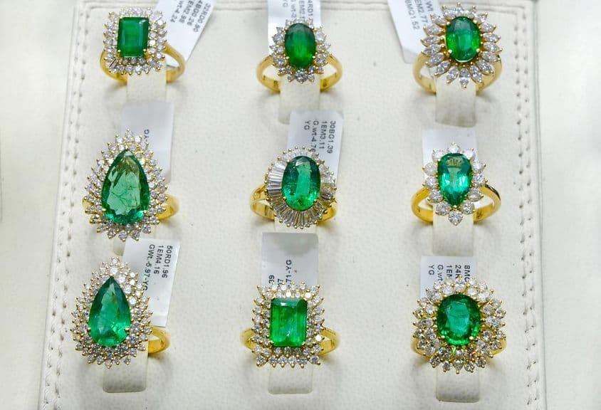 Anéis de esmeralda rodeados por diamantes em uma aliança de ouro.