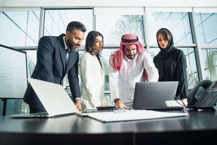 Executivos de empresa deliberando em um escritório com laptop e telefone à frente.