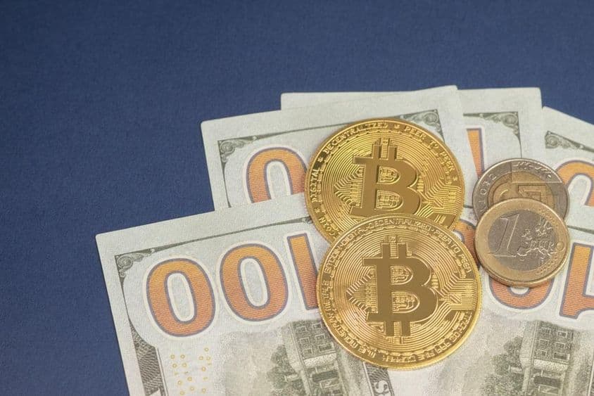 Dólar norte-americano sobre moedas de bitcoin ao lado de moeda de 1 euro