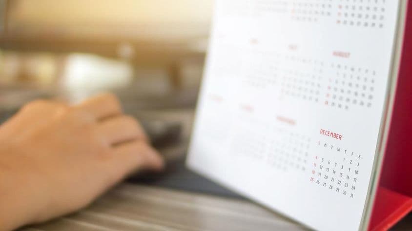 Uma mão ao lado de um calendário, com meses desfocados, dezembro claramente visível.