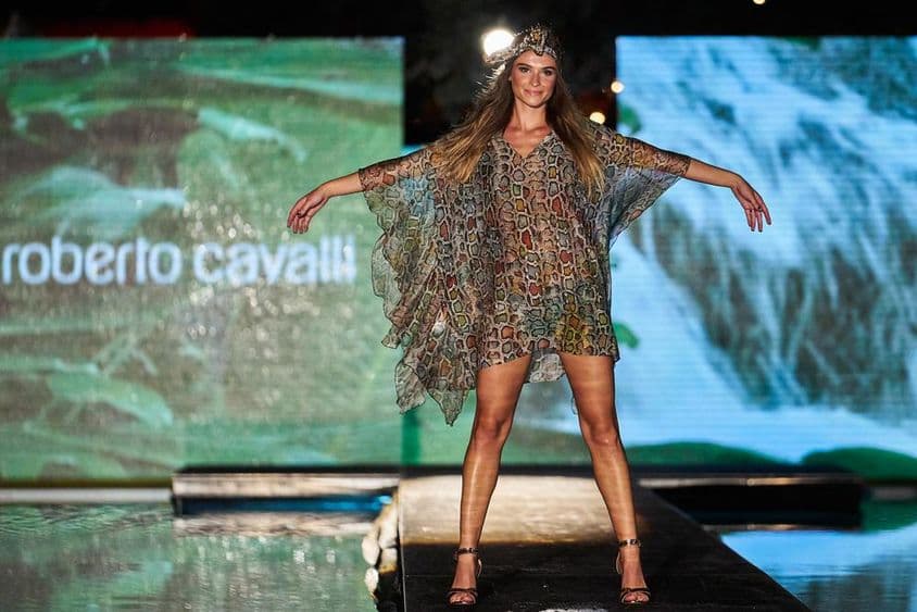 Sinal da Roberto Cavalli em destaque ao fundo, na frente uma figura feminina em um vestido Roberto Cavalli na passarela.