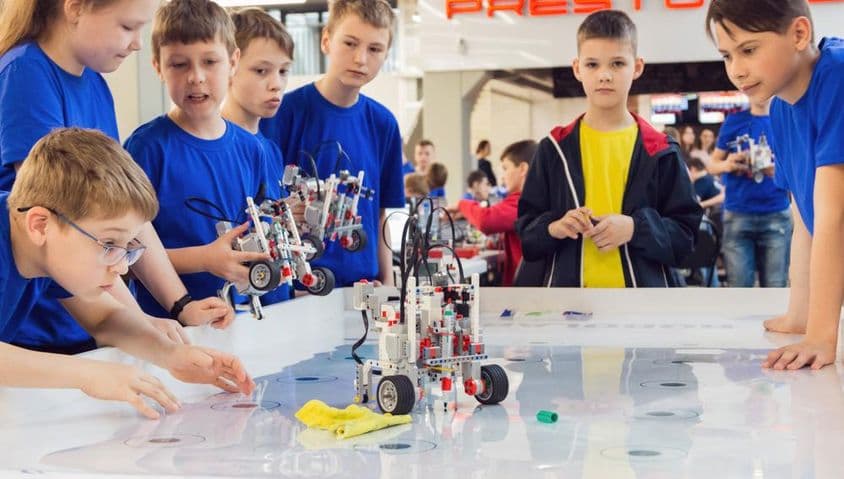 Estudantes com camisetas azuis construindo e programando um robô.