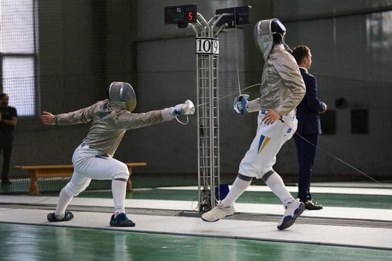 Dois esgrimistas competindo na pista, um marcando um ponto.