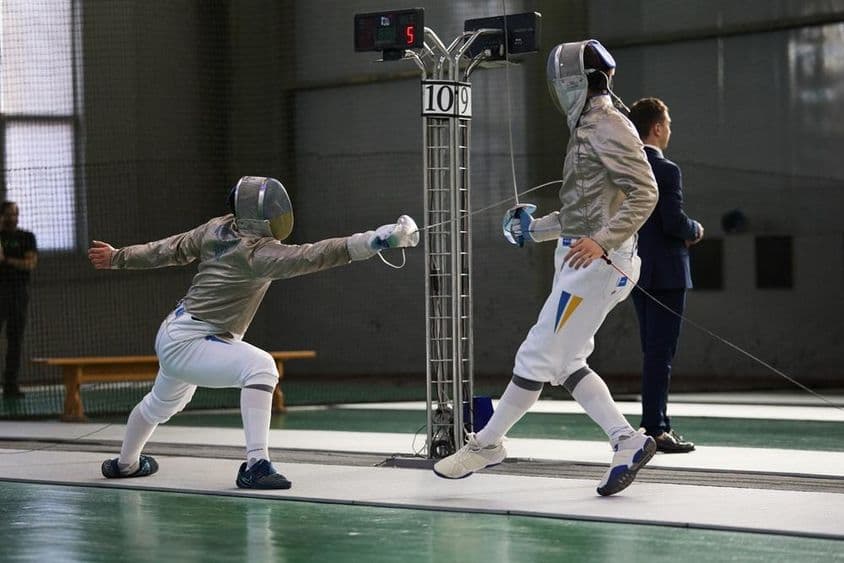 Dois esgrimistas competindo na pista, um marcando um ponto.