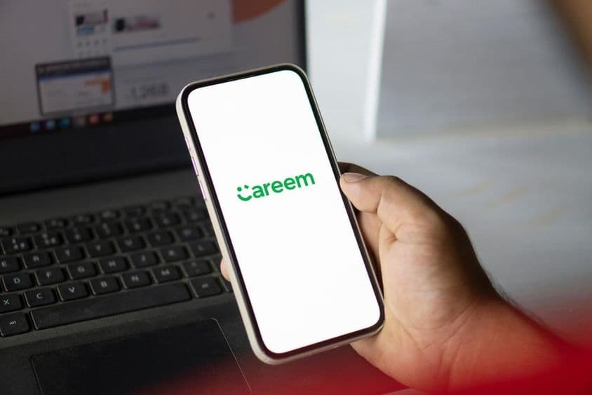 Uma mão segura um telefone rodando o aplicativo Careem, com um caderno visível ao fundo.
