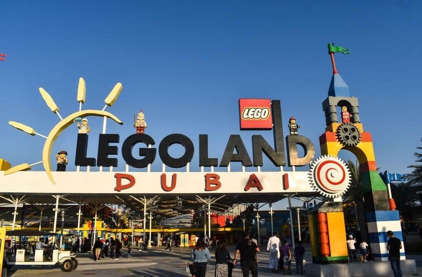 Entrada do LEGOLAND Dubai com pessoas e um carrinho de golfe na frente.