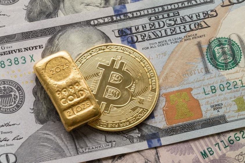 Uma barra de ouro de investimento e uma moeda de Bitcoin sobre uma nota de 100 dólares.