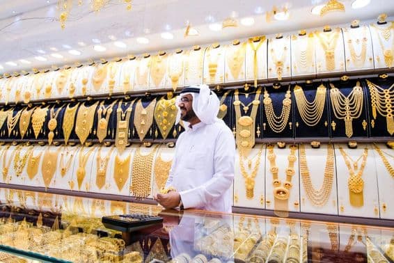 Vendedor de ouro em Dubai, com fundo de muitos colares de ouro, o vendedor em traje tradicional branco.