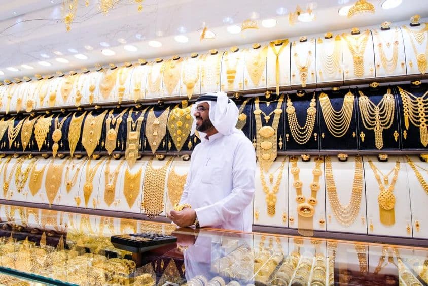 Vendedor de ouro em Dubai, com fundo de muitos colares de ouro, o vendedor em traje tradicional branco.