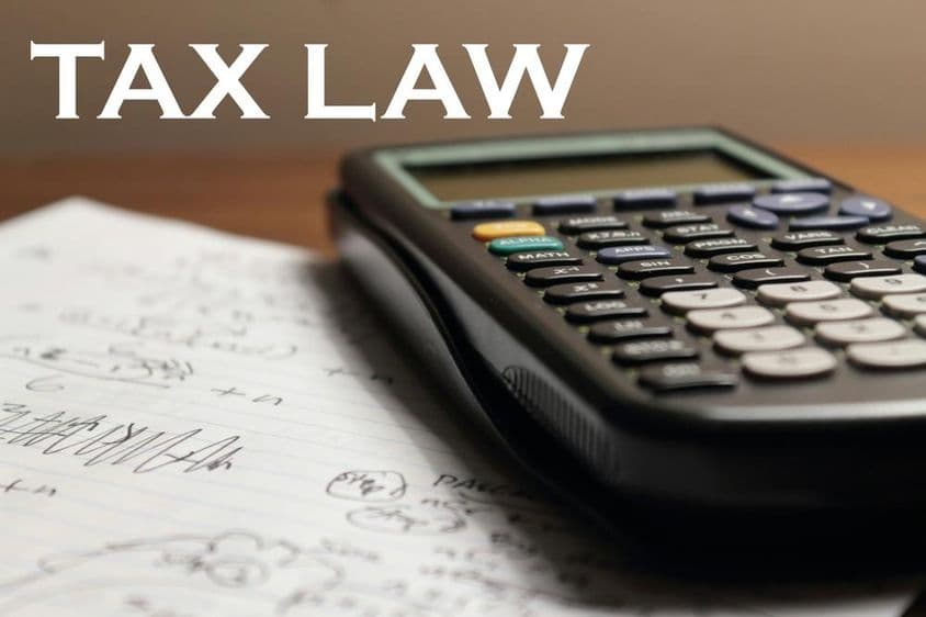 Uma calculadora em cima de um caderno com o rótulo legislação tributária acima dele.
