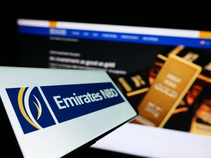 Sinalização do Emirates NBD em primeiro plano, ao fundo uma barra de ouro de investimento.