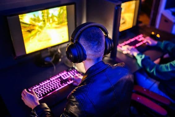 Gamers online visíveis, com teclado e monitor iluminados à frente.