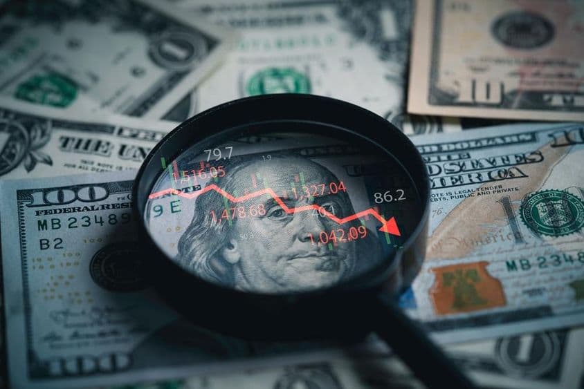 Notas de dólar com lupa mostrando queda na taxa de juros.