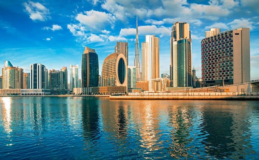 Arranha-céus de Dubai com água em primeiro plano, Burj Khalifa ao fundo.