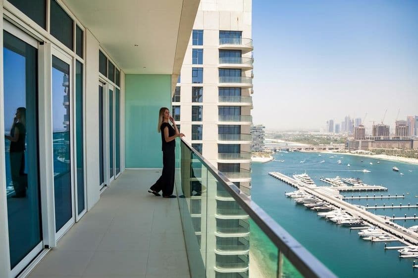 Uma mulher em um terraço em Dubai observando barcos no canal com um arranha-céu ao fundo.