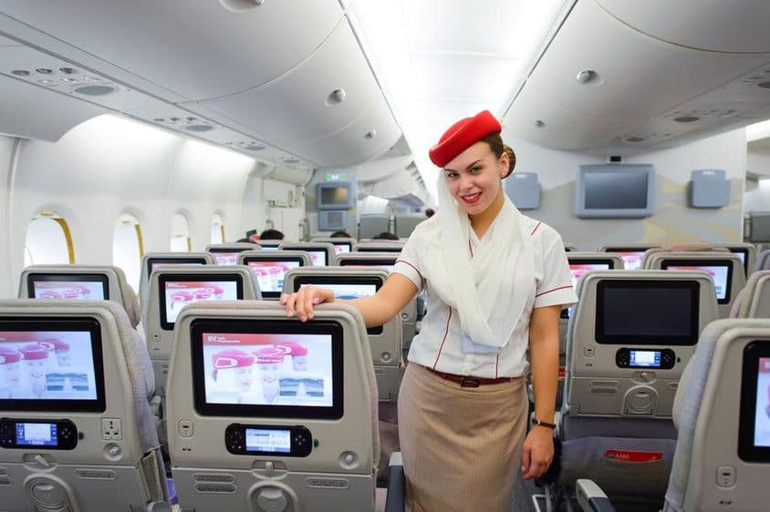 Interior de um avião Emirates com um comissário de bordo em destaque.