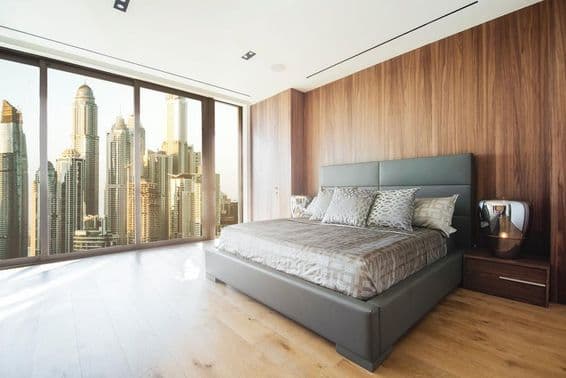 Interior de um quarto em Dubai com cama e vista de arranha-céus pela janela.