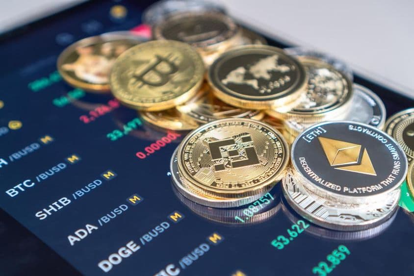 Moedas de Ethereum e bitcoin colocadas em uma tela de celular exibindo taxas de câmbio de criptomoedas.
