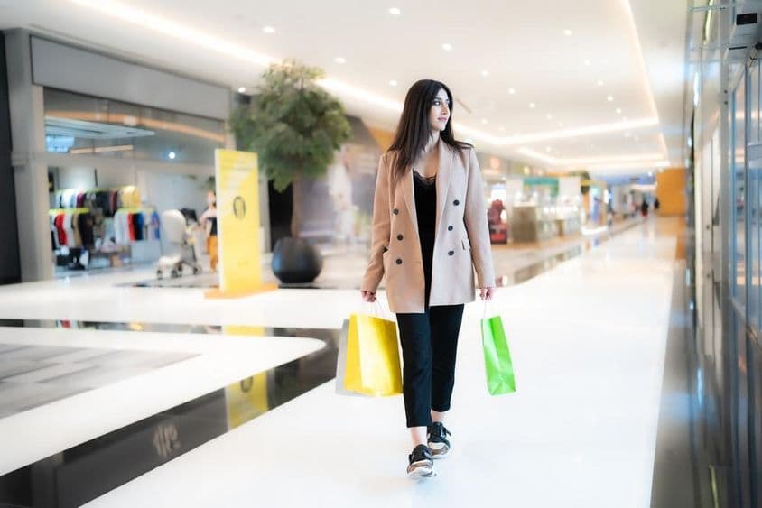 Uma mulher fazendo compras no Dubai Mall, segurando duas sacolas, com lojas ao fundo.