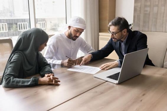 Uma família emiradense assinando um contrato na frente de um corretor, com um notebook na mesa.