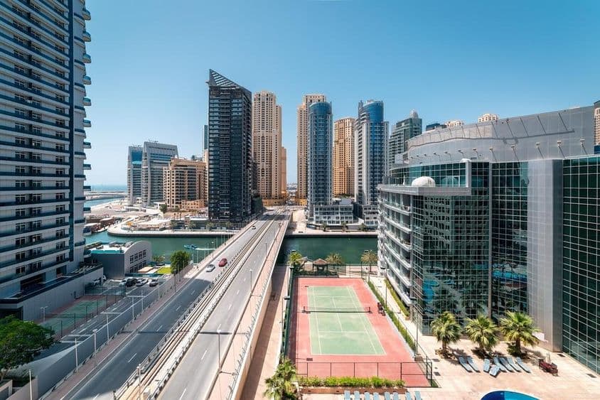 Uma quadra de tênis em Dubai com arranha-céus e uma lancha na água.