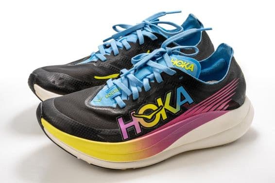 Um calçado esportivo Hoka com padrão colorido, predominantemente preto, com sola branca.