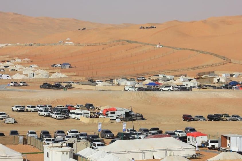 Cenário do Festival Internacional de Liwa no deserto com carros, trailers e tendas.