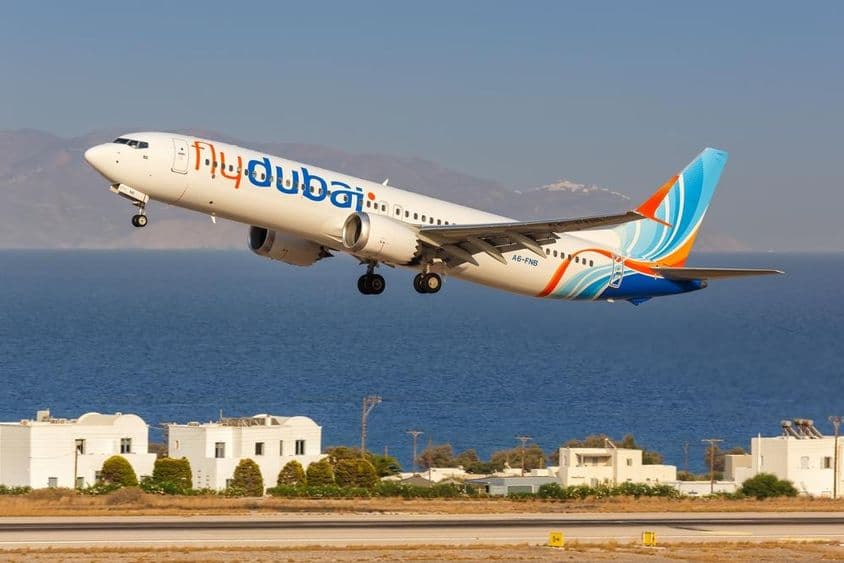 aeronave da flydubai voando a baixa altitude, com pequenas casas brancas e o mar ao fundo.