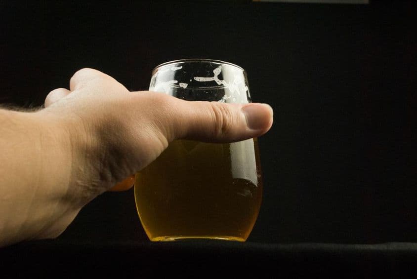 Uma mão segurando um copo de cerveja, com apenas a mão e o copo visíveis.