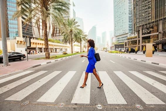 Em Dubai, uma mulher atravessa uma faixa de pedestres em uma estrada vazia, com casas visíveis ao fundo.