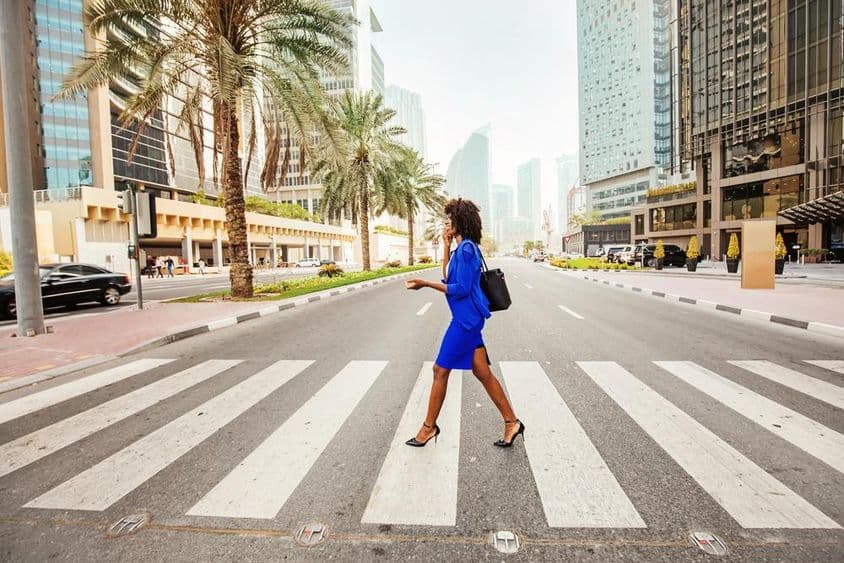 Em Dubai, uma mulher atravessa uma faixa de pedestres em uma estrada vazia, com casas visíveis ao fundo.