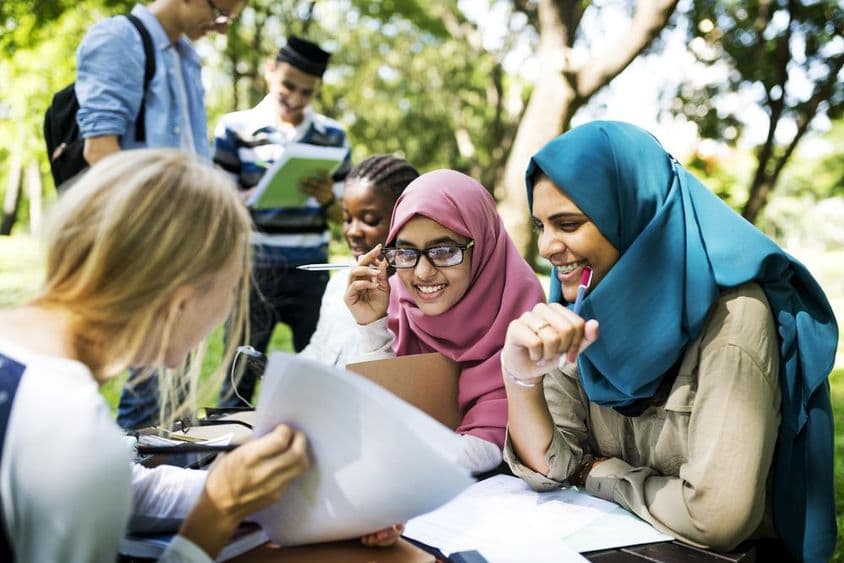 Estudantes em Dubai escrevendo lições e conversando ao ar livre.