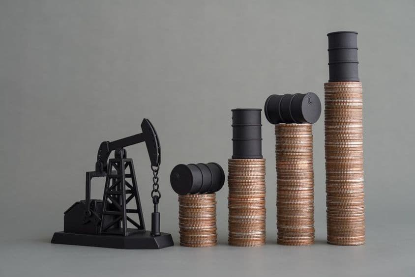 Mini plataforma de petróleo e moedas empilhadas com um barril de petróleo no topo.