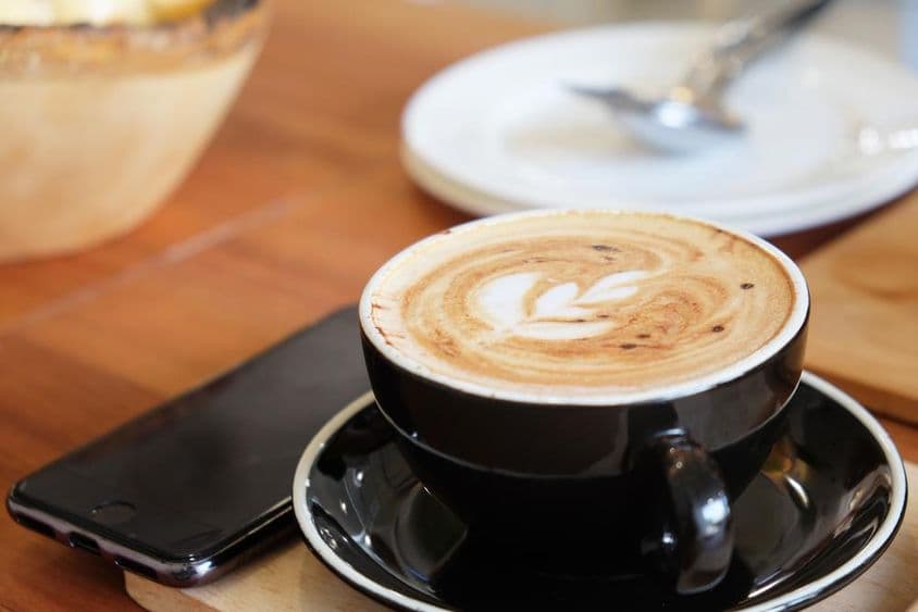 Uma xícara de cappuccino sobre a mesa com um telefone ao lado.