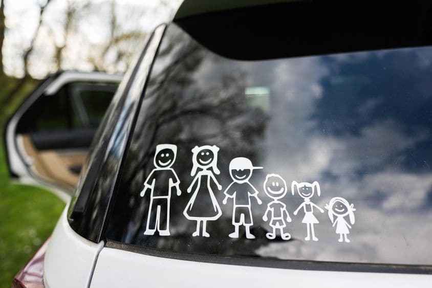 A janela traseira de um carro exibe um adesivo de uma família, incluindo 2 adultos e 4 crianças.