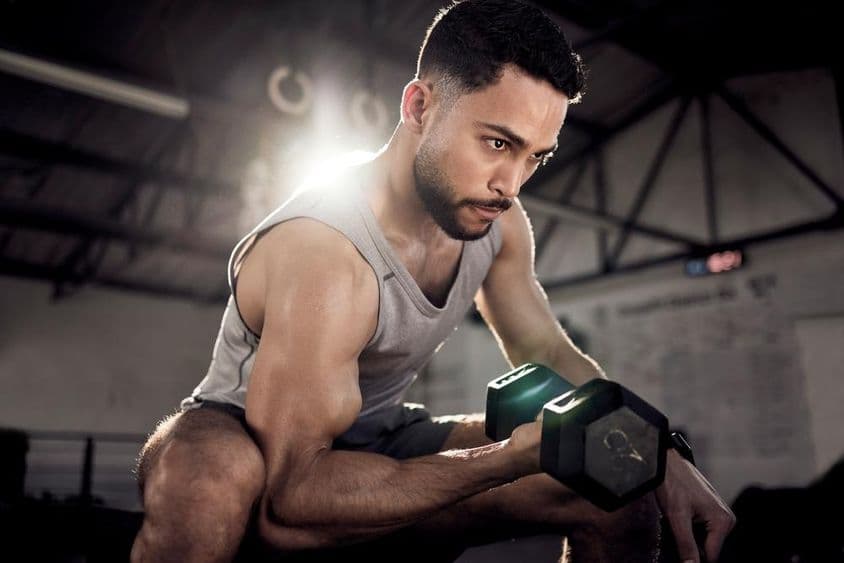 Um homem musculoso fortalecendo seus bíceps com um pequeno haltere em uma academia.
