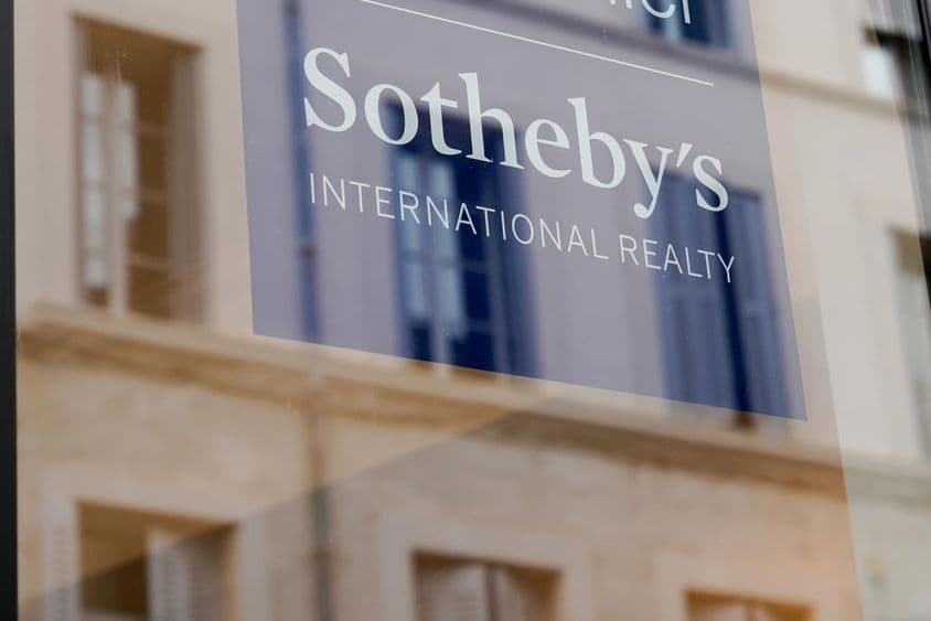 Placa da Sotheby's visível na fachada de um prédio, em um painel transparente.