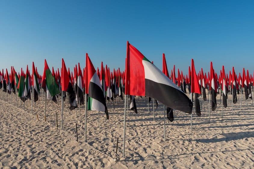 Bandeiras dos EAU plantadas em uma praia.