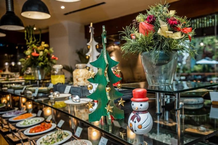 Pequeno boneco de neve em um restaurante sobre o balcão de vegetais, ao lado de uma árvore de Natal de madeira.