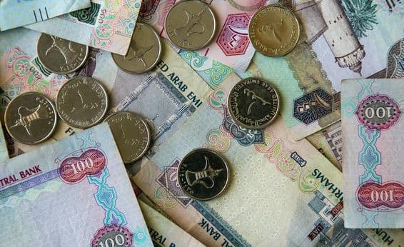 Notas de papel Dubai espalhadas sobre uma mesa com moedas de 1 dirham acima.